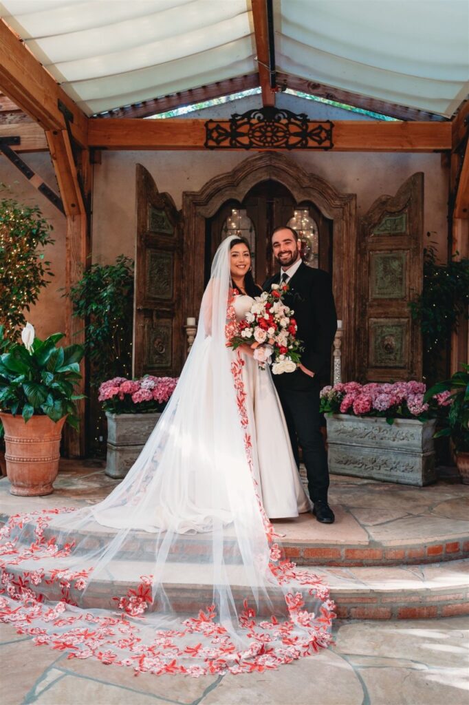 bride wearing satin ballgown wedding dress with red lace edge veil