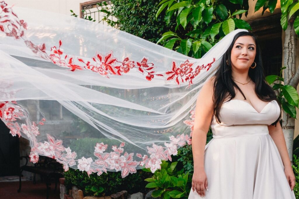 bride wearing satin ballgown wedding dress with red lace edge veil