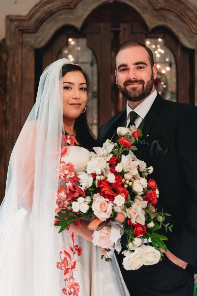 bride wearing satin ballgown wedding dress with red lace edge veil