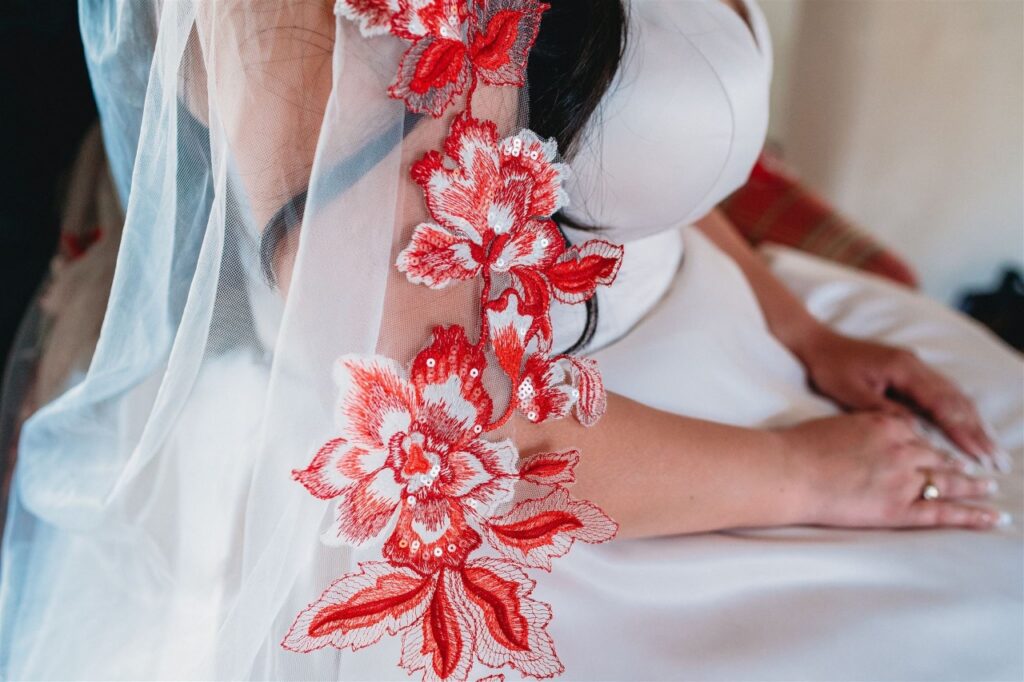 bride wearing satin ballgown wedding dress with red lace edge veil