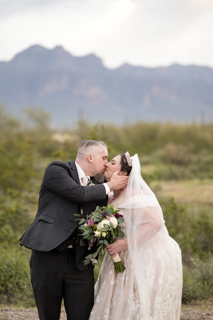 plus size bride wearing champagne and lace wedding dress while groom in black tux kisses her at arizona outdoor wedding